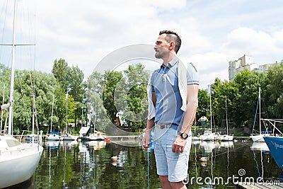 Handsome man on vacation with yachts on river pier and forest. Stock Photo