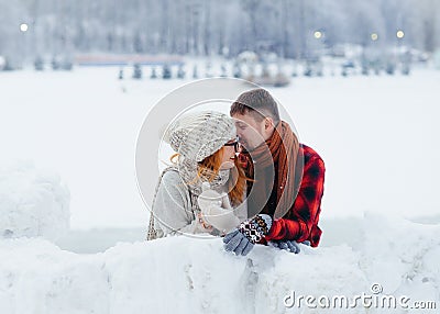 The handsome man is whispering something funny in the ear of his laughing girlfriend. Winter village location. Stock Photo