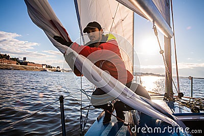 Handsome man on yacht touches white sail called assymetric spinnaker, works with tackle in sea at summer day, under view Stock Photo