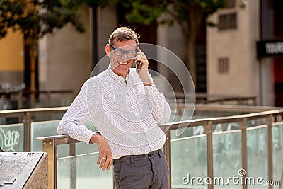 Handsome mature creative freelance businessman talking on the mobile phone and smiling while walking outdoor urban area in the Stock Photo