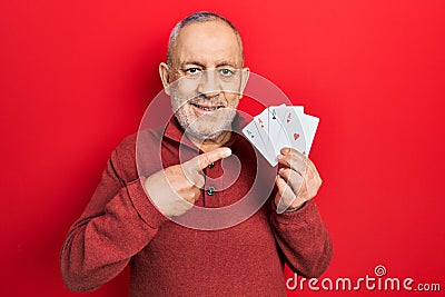 Handsome mature man playing poker holding cards smiling happy pointing with hand and finger Stock Photo