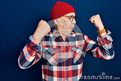Handsome mature man wearing hipster look with wool cap showing arms muscles smiling proud Stock Photo