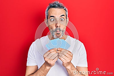 Handsome middle age man with grey hair covering face with cards making fish face with mouth and squinting eyes, crazy and comical Stock Photo