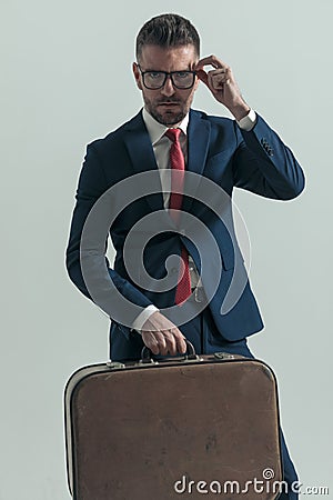 Handsome middle aged businessman holding luggage and fixing glasses Stock Photo
