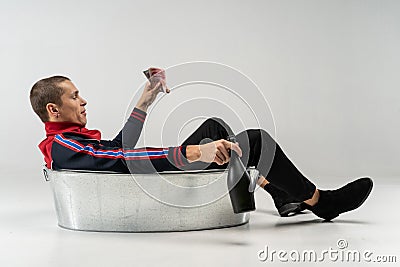 Handsome model male with short haircut in casual wear sitting in the metal bath in studio Stock Photo