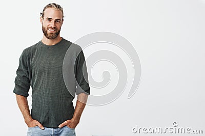 Handsome nordic man with beard and stylish hairstyle in grey shirt and jeans smiling, looking in camera, keeps hands in Stock Photo