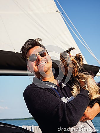 Handsome person hugs his small dog yorkshire terrier on a sailing yacht during vacations Stock Photo