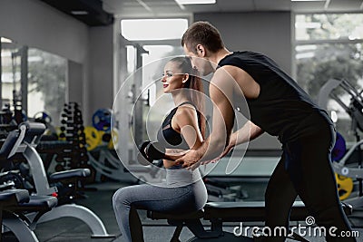 Handsome personal instructor helping his female client to training with dumbbells. Stock Photo