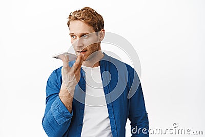 Handsome redhead man record voice message, holding smartphone near lips as translating his words in cellphone app, using Stock Photo