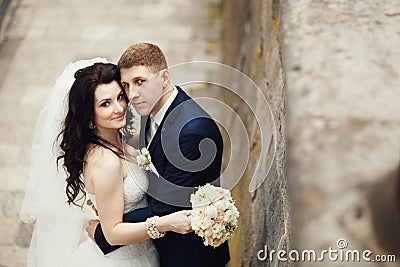Handsome romantic groom kissing beautiful brunette bride near old wall castle Stock Photo