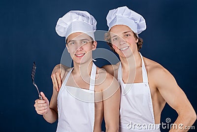 Two handsome chefs with apron on naked muscular body with kitchen utensils on blue background Stock Photo