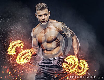 Handsome shirtless tattooed bodybuilder with stylish haircut and beard, wearing sports shorts, posing in a studio. Fire Stock Photo