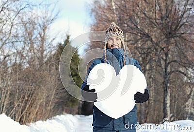 Handsome smiling bearded hipster man holding a big heart made of snow, standing on snowy road in winter park. Fall in love. Stock Photo