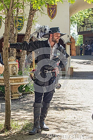 Handsome smiling man dressed all in black leather with sword and hat and feather and boots standing by tree at the Oklahoma Renais Editorial Stock Photo