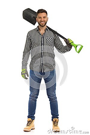 Handsome smiling man in lumberjack shirt is standing with spade on his shoulder. Front view. Studio shot Stock Photo