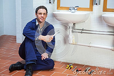 Handsome smiling plumber sitting next to sink holding wrench Stock Photo