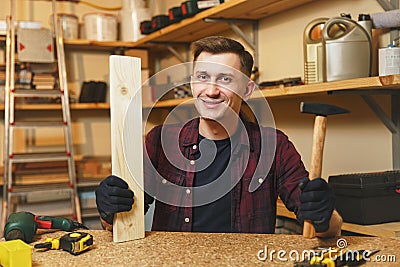 Handsome smiling young man working in carpentry workshop at wooden table place with piece of wood Stock Photo