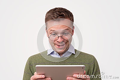 Handsome surprised young man wearing green sweater looking on tablet Stock Photo