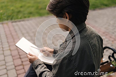 Handsome teenager painting something in his notepad outdood during the break. Talanted young boy Stock Photo