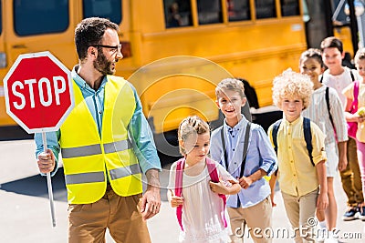 handsome traffic guard crossing road with pupils in front of Stock Photo