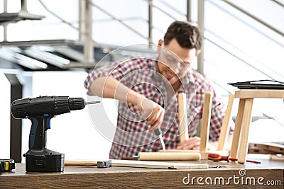 Handsome working man repairing wooden stool at table indoors Stock Photo