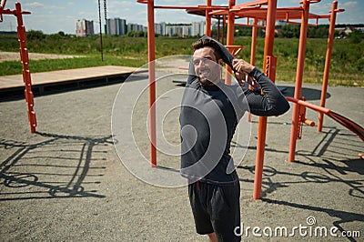 Handsome young adult 40 years old European sporty man stretching arms behind his back before training on the sportsground in open Stock Photo