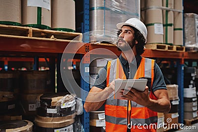 Handsome young bearded man wearing safety vest and hard hat using digital tablet entering data in warehouse standing Stock Photo