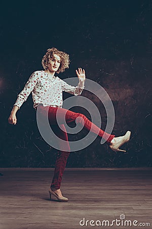 A handsome young blond man androgyne in the image of a woman in a blouse with flowers, expressively waving his arms and legs Stock Photo