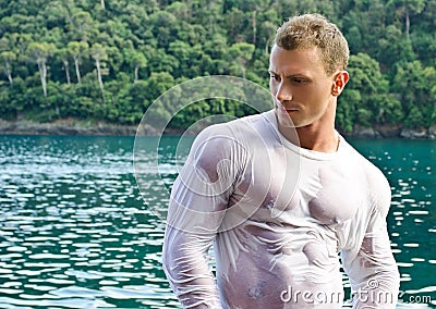 Handsome young bodybuilder by the sea with wet shirt on Stock Photo