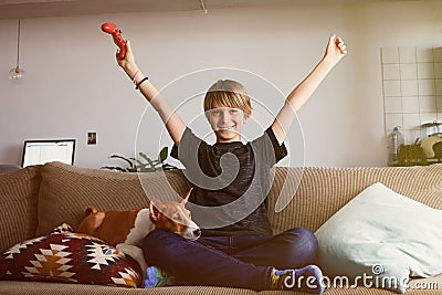 Handsome young boy celebrating his victory in video game console seated on a sofa with basenji dog puppy sleeping close Stock Photo