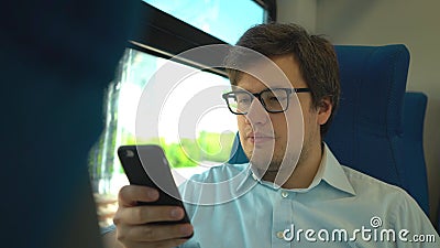 Handsome young businessman wearing a blue shirt and glasses is riding a train dialing a number and talking on his phone Stock Photo