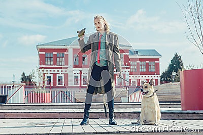 A handsome young guy in a khaki and berets military coat walks with a big dog. Holds a flask in his hand Stock Photo