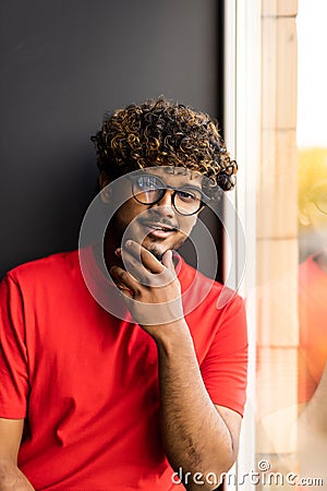 Handsome young indian man sits home on windowsill Stock Photo