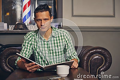 Handsome young man in a barbershop is waiting for the master in the waiting room while drinking coffee Stock Photo