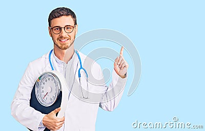 Handsome young man with bear as nutritionist doctor holding weighing machine surprised with an idea or question pointing finger Stock Photo