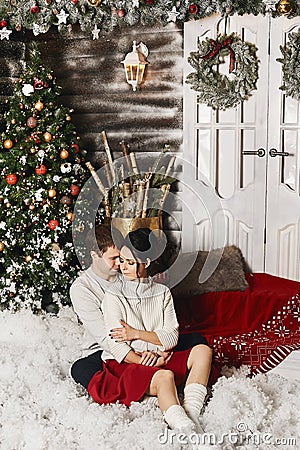 Handsome young man and beautiful model girl sit on the stairs at winter exterior of a country house with Christmas Stock Photo