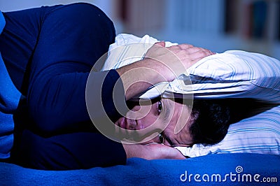 Handsome young man in bed with eyes opened suffering insomnia and sleep disorder thinking about his problem coverinh his Stock Photo