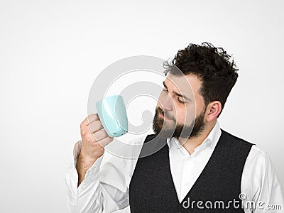 Handsome, young man with black beard posing with turquoise coffee cup or tea cup in front of white background Stock Photo