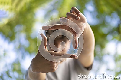 A handsome young man blinks his eyes and looks through a frame made up of hands Stock Photo
