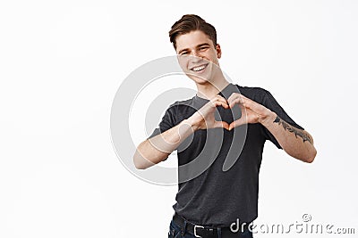 Handsome young man, boyfriend shows I love you heart sign and smiles cute at you, laughing while confessing his feelings Stock Photo