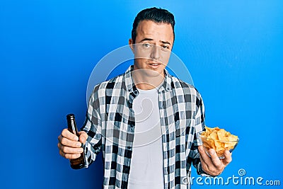 Handsome young man drinking a pint of beer holding chips clueless and confused expression Stock Photo