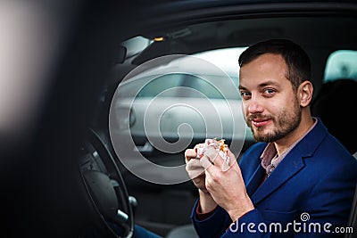 Handsome young man eating a hurried lunch in his car Stock Photo