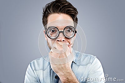 Handsome young man with funny glasses joking and making funny face over gray background. Stock Photo