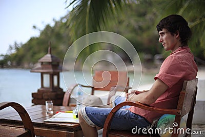 Handsome young man in sits in beach cafe by sea has vacation time. Travel concept. Stock Photo