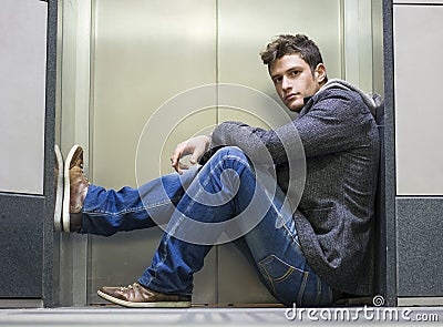 Handsome young man sitting in front of elevator doors Stock Photo