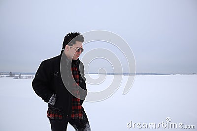 Handsome young man in sunglasses stands in a field in winter. stands on a hill and looks into the distance. the majestic sky in th Stock Photo