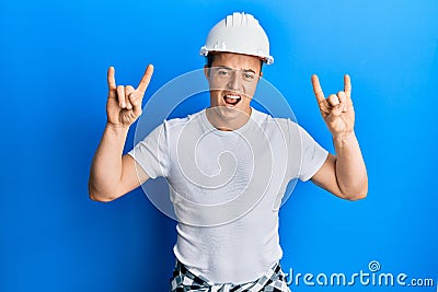 Handsome young man wearing builder uniform and hardhat shouting with crazy expression doing rock symbol with hands up Stock Photo