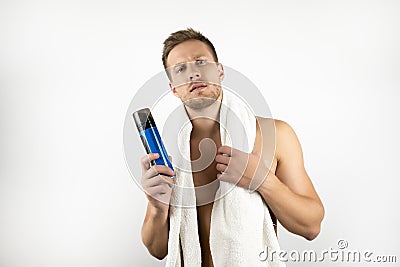 Handsome young man with white towel on his shoulders holding shaving foam in his hand doing his morning routine on Stock Photo