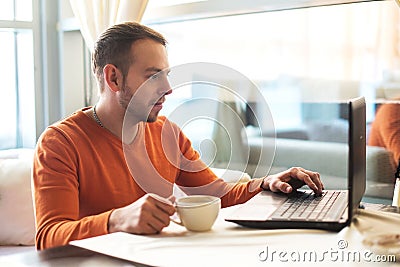 Handsome young man working on notebook, thinking, while enjoying coffee in cafe Stock Photo