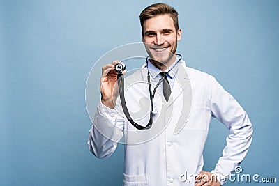 Handsome young medic holding a stethoscope, isolated over light blue. Stock Photo